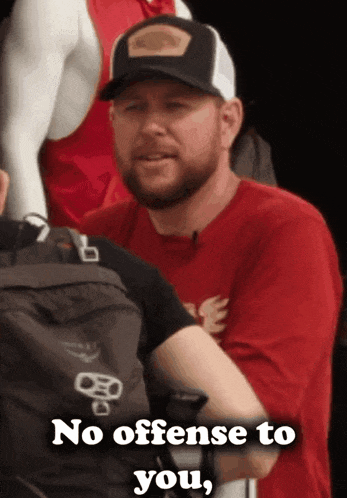 a man wearing a red shirt and a black hat says no offense to you