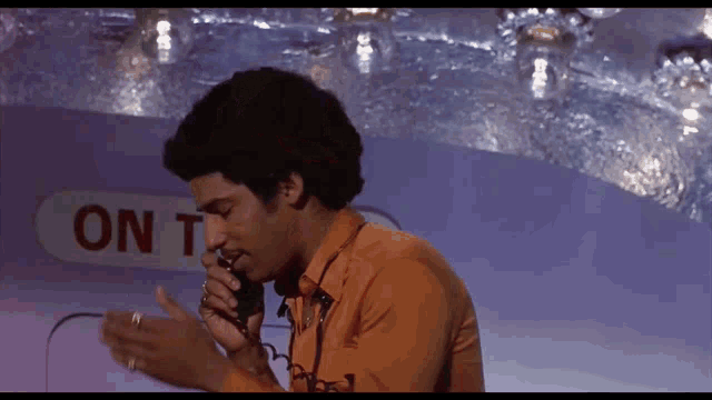 a man speaking into a microphone in front of a sign that says on tv