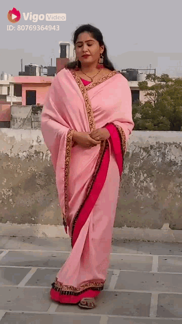a woman wearing a pink saree is standing on a rooftop .