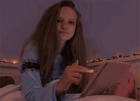 a girl laying on a bed reading a book and pointing at it