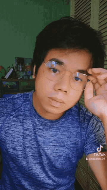 a young man wearing glasses and a blue shirt with tik tok written on the bottom