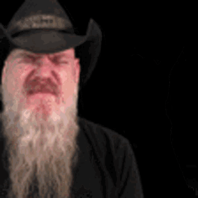 a man with a beard wearing a cowboy hat and a black shirt is crying .