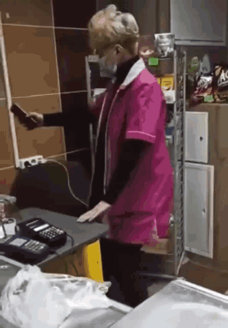 a woman wearing a mask and a pink apron is standing at a counter in a store