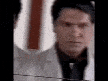a man in a white coat and black tie is looking at himself in the mirror .
