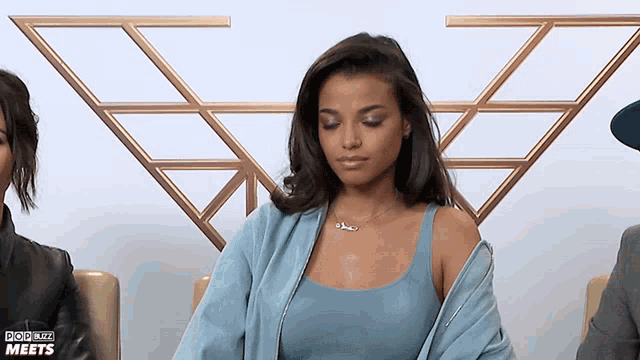 a woman in a blue tank top is sitting in front of a sign that says " pop biz meets "