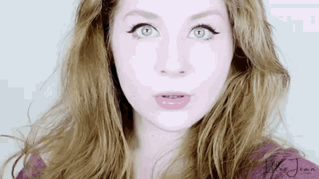 a close up of a woman 's face with long hair and a surprised look on her face .