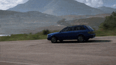 a blue car is driving down a road in front of a mountain