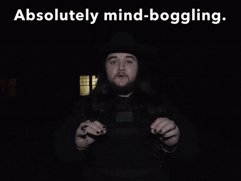 a man with long hair and black nails stands in the dark with the words " absolutely mind-boggling " below him