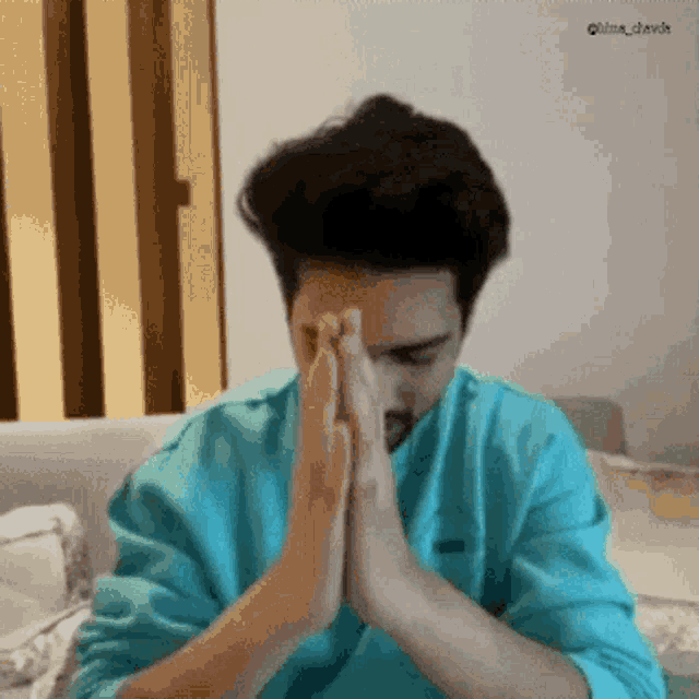 a man in a blue sweatshirt is praying with his hands folded in front of his face .