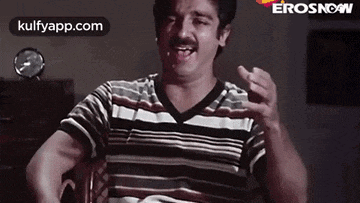 a man in a striped shirt is sitting in a chair and making a face .