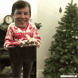 a man wearing a merry christmas sweater is holding a basket of candy canes in front of a christmas tree