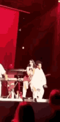 a woman singing into a microphone on a stage with a red curtain in the background