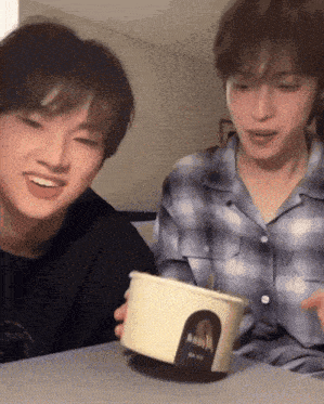 two young men are sitting at a table and one of them is holding a container that says ' aquafina '