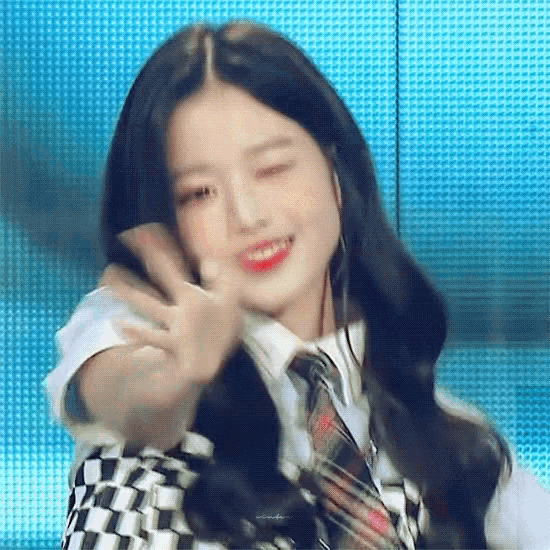 a girl in a plaid shirt and tie is making a peace sign with her hand .