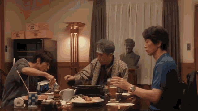 three men are sitting at a table with a statue in the background that has the letter a on it
