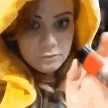 a close up of a woman wearing a yellow hoodie and holding a red object .