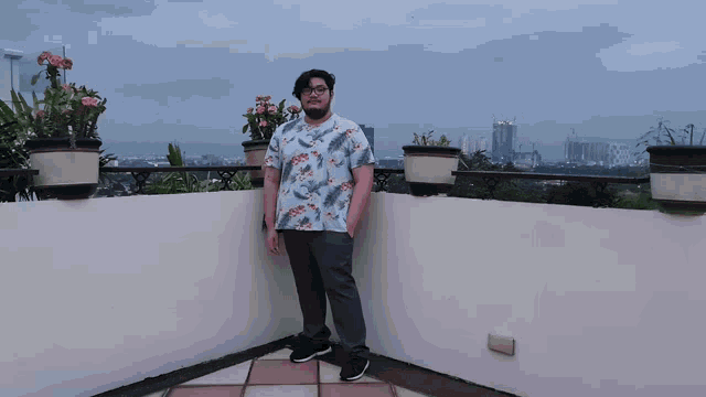 a man in a floral shirt stands on a balcony overlooking the city