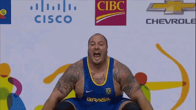 a man in a blue shirt with the word brasil on it is squatting down in front of cisco and chevrolet logos