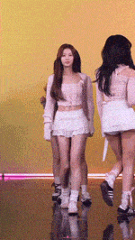a group of girls are walking on a stage and one of them is wearing a white skirt
