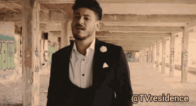 a man in a suit is standing in a hallway with graffiti on the walls and the words @tvresidence above him