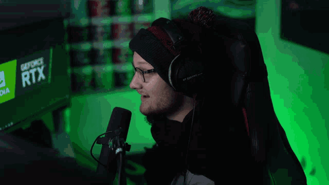 a man wearing headphones stands in front of a microphone in front of a geforce rtx monitor