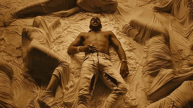 a shirtless man laying on a bed surrounded by white sheets