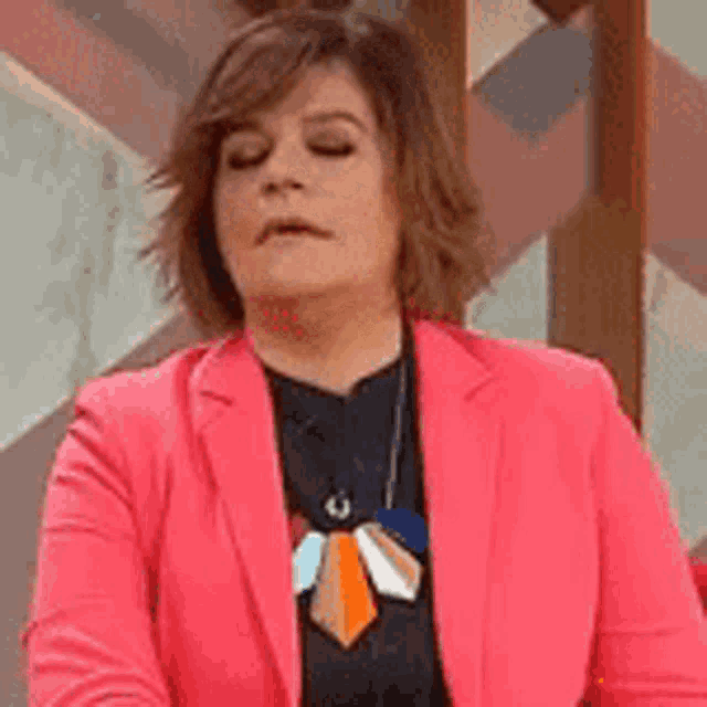 a woman wearing a pink jacket and a tie is sitting with her eyes closed .