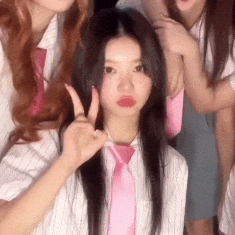 a girl wearing a pink tie is making a peace sign .