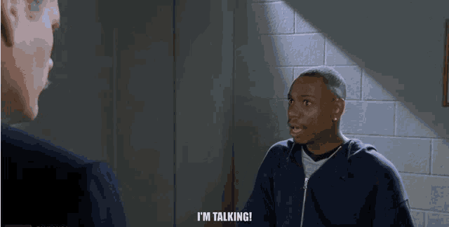 a man in a blue sweatshirt is talking to another man in a suit