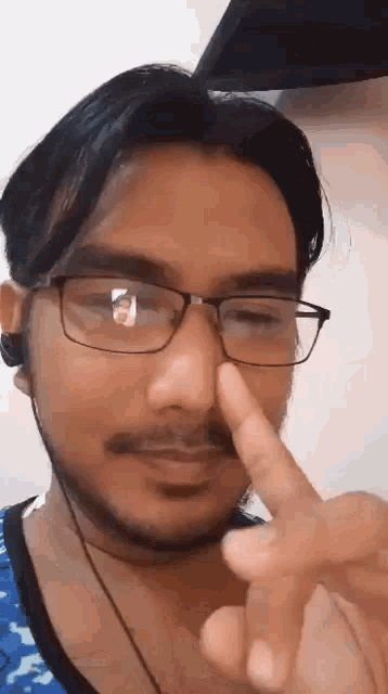 a man wearing glasses and ear buds is holding his nose .