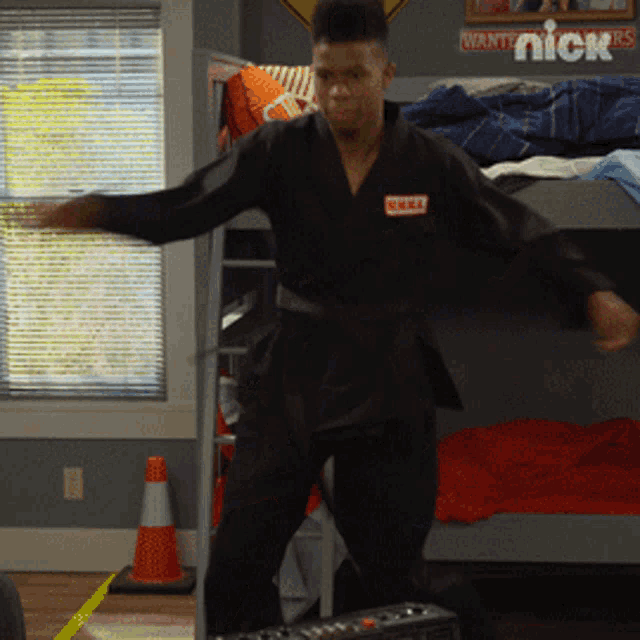 a man in a black karate uniform is dancing in a bedroom with a sign that says nick on it