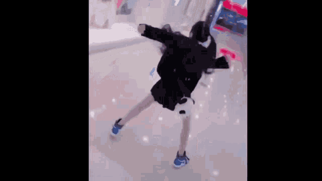 a young girl is standing in a mall wearing a black jacket and blue shoes .