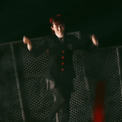 a woman is dancing in front of a chain link fence in a dark room .