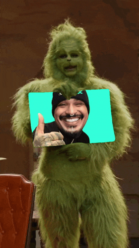 a grinch holding a picture of a man with a mustache