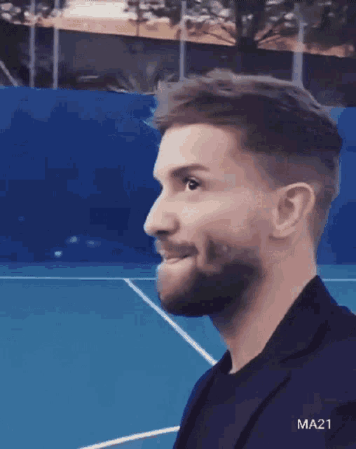 a man with a beard is standing in front of a tennis court with the hashtag ma21