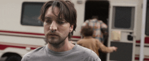a man with a nose ring is standing in front of a camper .