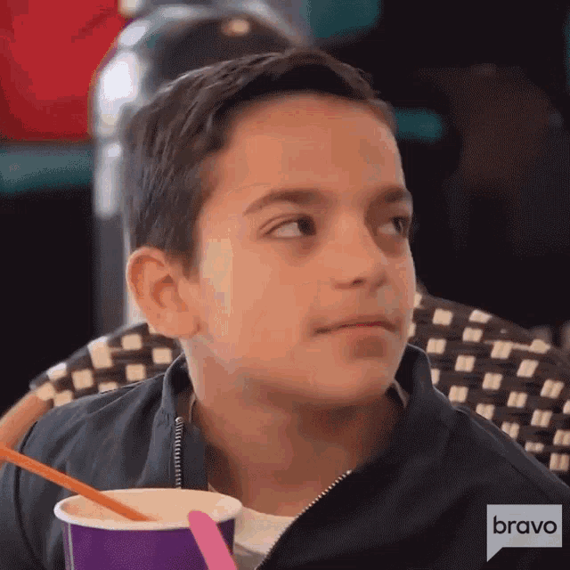 a young boy is sitting at a table with a bravo logo on his jacket