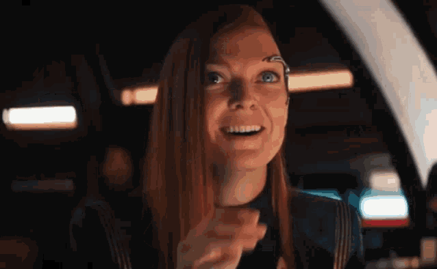 a woman with long red hair is smiling while sitting in a car in a dark room .