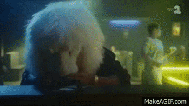 a man with white hair is sitting at a table in a dark room with a makeagif.com logo in the corner .
