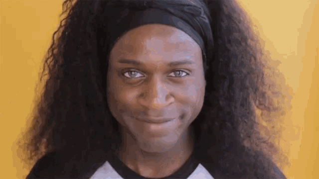 a man with long curly hair and a headband is smiling .