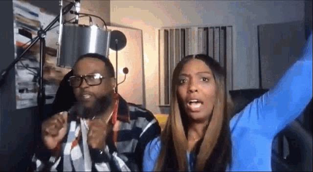 a man and a woman are standing in front of a microphone with their arms outstretched .