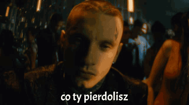 a man with a tattoo on his forehead is surrounded by people and the words " co ty pierdolisz " are above him