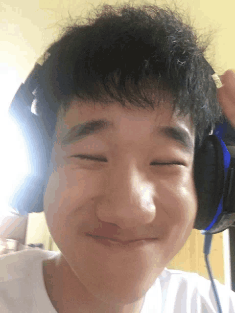 a young man wearing headphones looks at the camera with his eyes closed
