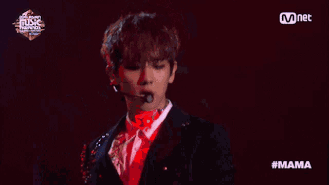 a man wearing a suit and a microphone stands in front of a screen that says mnet