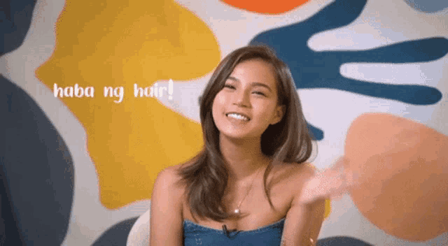 a woman says " haba ng hair " in front of a colorful painting