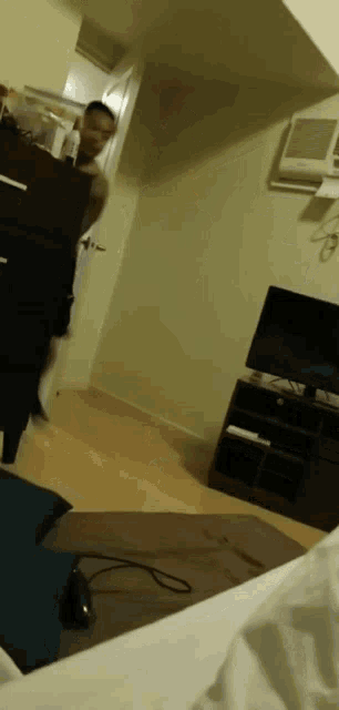a person is standing in a room with a tv and a dresser .