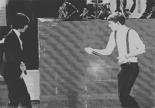 a black and white photo of two men dancing in front of a wall that says direction