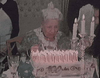 an elderly woman is blowing out candles on a cake .