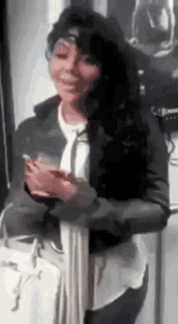 a woman in a leather jacket and tie is smiling and holding a cell phone .