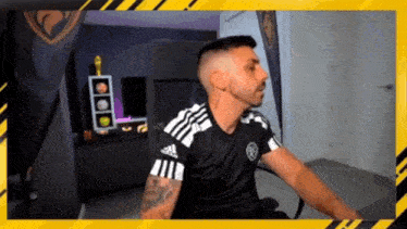 a man in a black and white adidas shirt is sitting in a chair